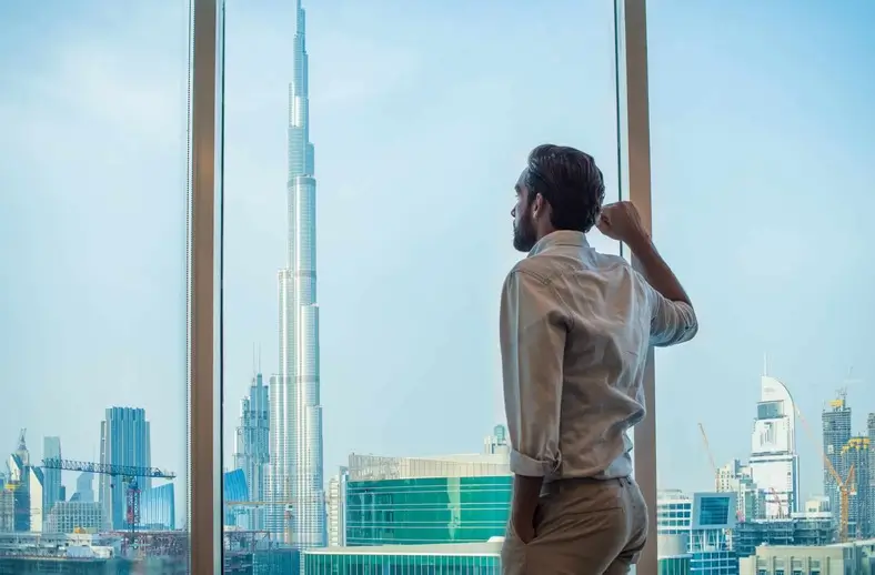 Homme d'affaires contemplant la ville de Dubaï depuis sa fenêtre – dropshipping à Dubaï