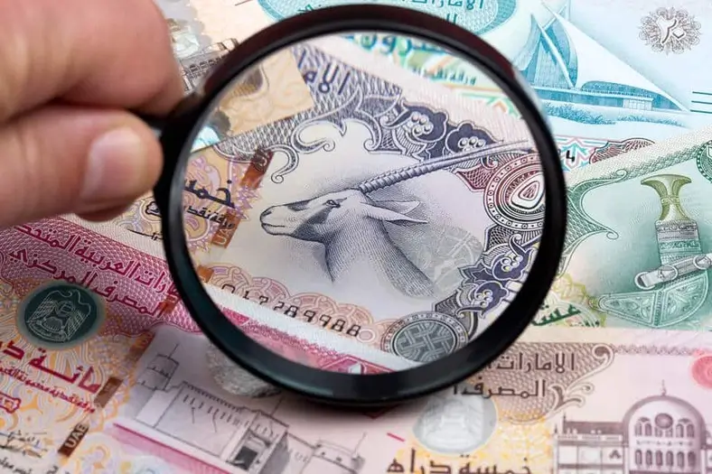 Loupe examinant des dirhams de Dubaï pour analyser les revenus à déclarer aux autorités fiscales