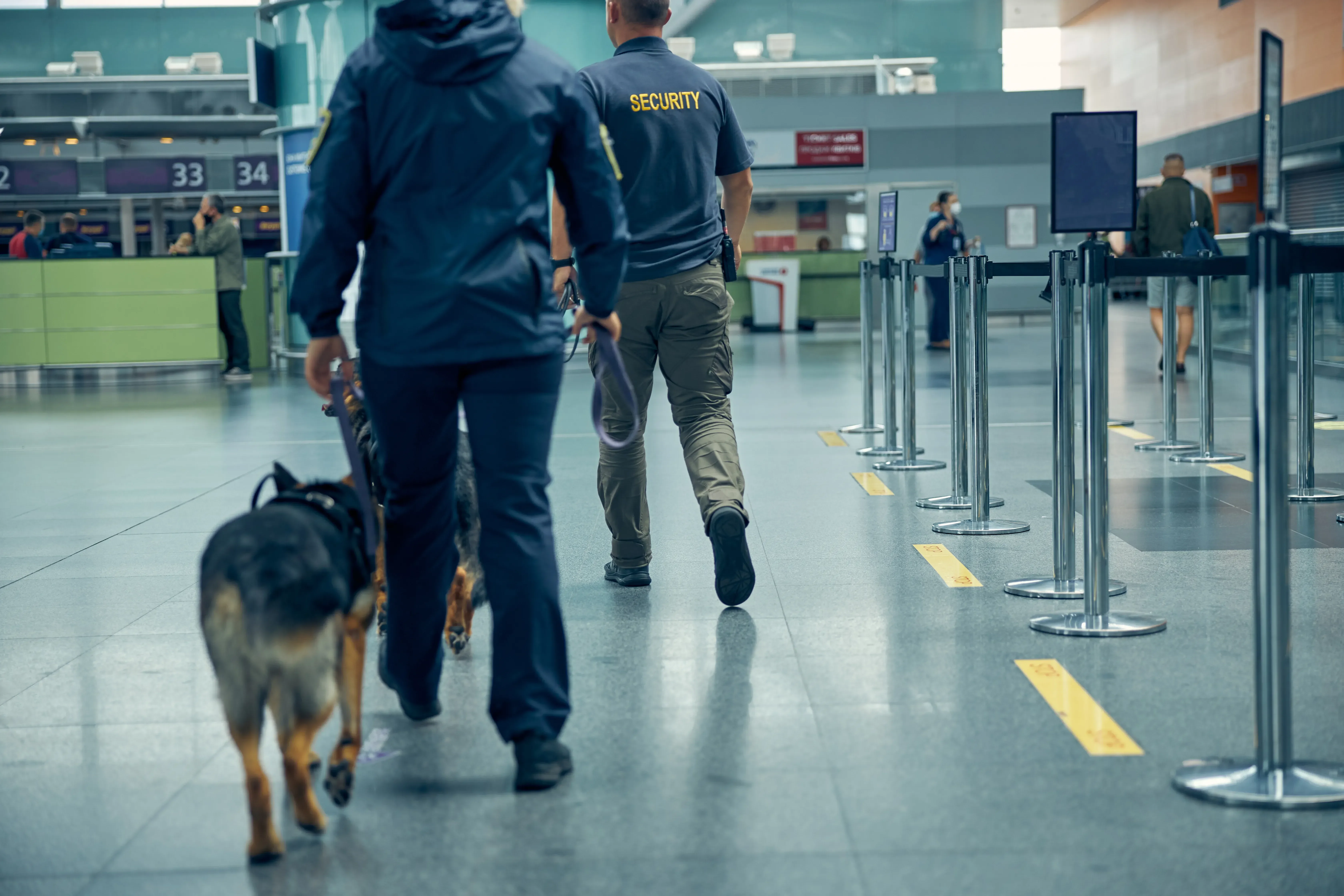 Contrôles de sécurité à l’aéroport et blocages d’entrée à Dubaï Agents de sécurité et chien de contrôle patrouillant dans un hall d’aéroport, illustrant les contrôles et blocages possibles à l’entrée à Dubaï.