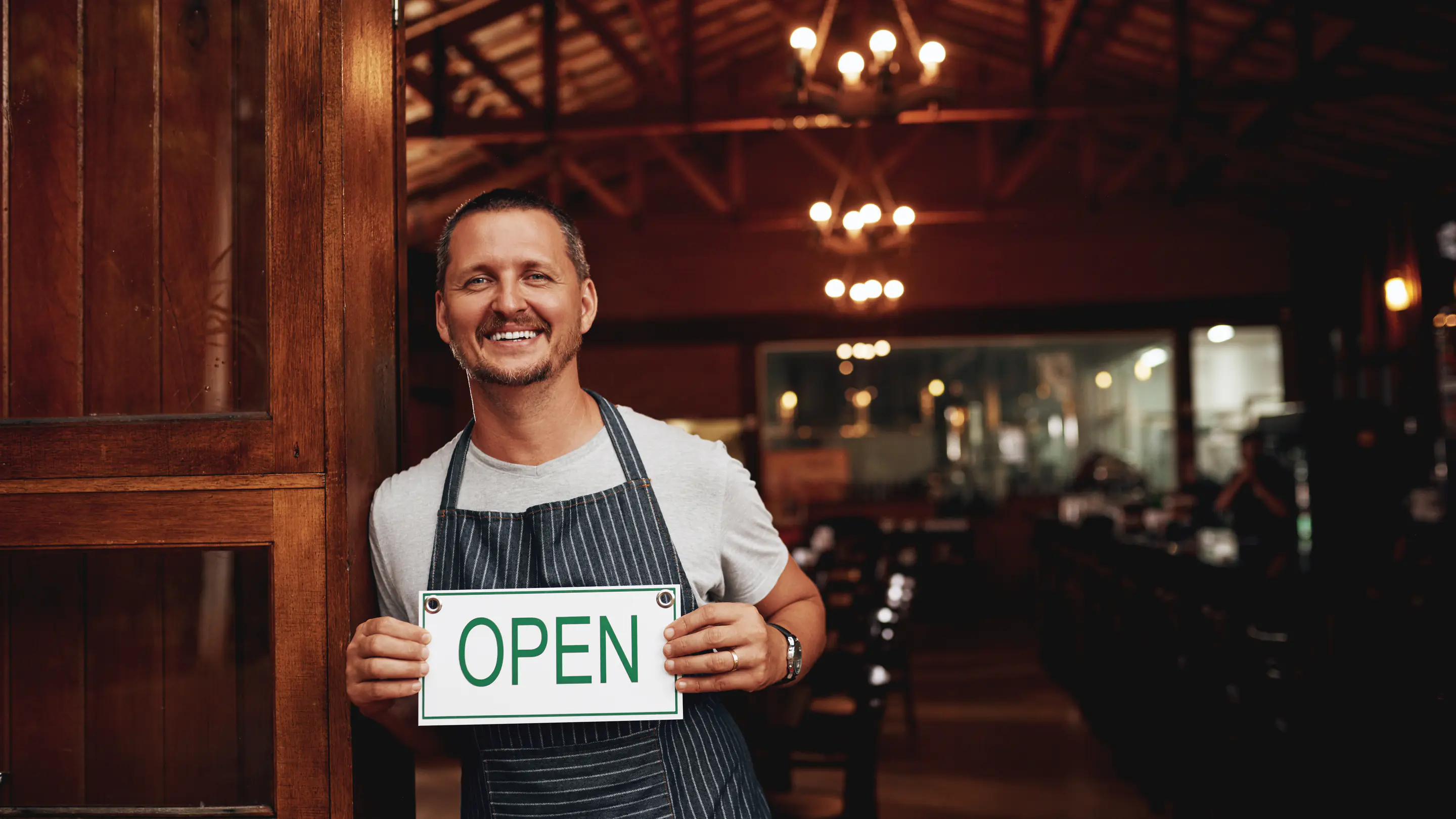 Restaurateur tenant un panneau OPEN à l’entrée de son restaurant
