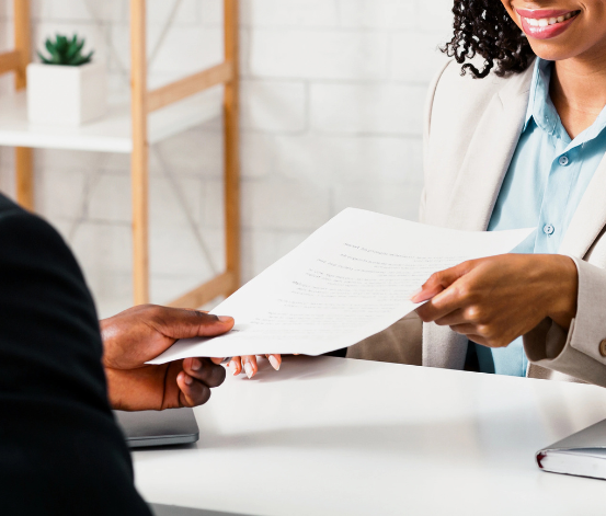 Une femme professionnelle souriante tend un document blanc à un homme assis à une table de bureau moderne, représentant un entretien d'embauche